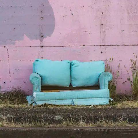 A blue sofa left outside against a pink wall