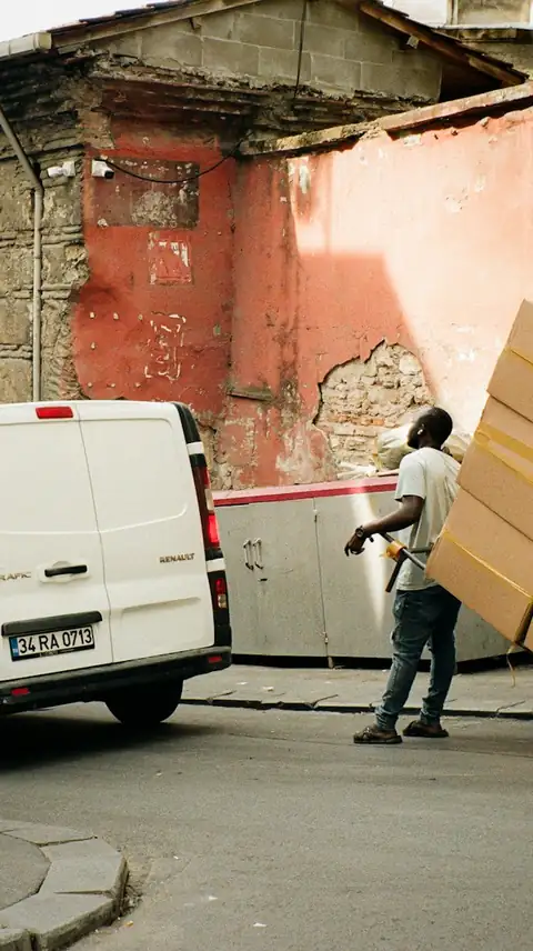 A worker wheeling boxes on a hand truck beside a white van